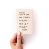 What to Write in Any Card Zine shown held against white background, displaying inspirational text about card writing on a soft pink page. Small, compact guide with handwritten-style text offers simple advice about sending heartfelt messages.