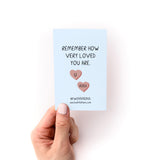A light blue card from the "Things to Do When You're in a Depressive Spiral Zine" showing handwritten text "Remember how very loved you are" with two heart-shaped illustrations in pink, held against a white background. The Kwohtations branding appears at the bottom.