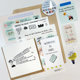 For anyone trying to work while the world is on fire" care package featuring motivational stickers, magnets, postcards, and a 'Working is Hard' zine laid out on white surface, displaying encouraging messages and cute illustrations in pastel colors. Package includes self-care themed items and inspirational notes.