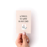 What to Write in Any Card Zine shown as a small peach-colored booklet held against a white background, featuring minimalist text and a small heart icon with writing illustration. The cover displays "6 Things to Write in Any Card" in simple black lettering.