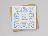 Square greeting card featuring light blue illustrations of winter-themed items including mittens, hats, socks, candles, mugs, vases, and books arranged around the text "Merry and Happy Everything," paired with a kraft paper envelope.