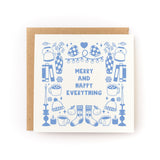 Square greeting card with light blue illustrations of cozy winter items including mittens, mugs, candles, books, hats, socks, and vases, surrounding the text "Merry and Happy Everything," paired with a brown kraft envelope.