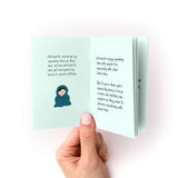 Inside spread of How to Care For Your Introvert Zine showing a small illustration of a person wrapped in a cozy blanket on mint green pages, with handwritten text explaining how introverts recharge through alone time versus social settings. Hand holding the open booklet shows its compact size.