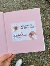 Welcome to the Grief Club: Signed Book + Sympathy Card - Open pink book page showing author Janine Kwoh's signature with illustrated hands holding cups, featuring the book title and author's signature against a soft pink background.