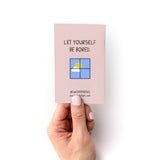 30 Things to Do Instead of Looking at Your Phone Zine shown as a small pink booklet held in hand, featuring text 'Let Yourself Be Bored' and a simple window illustration with a yellow sun against blue sky. Branding for Kwohtations visible at bottom.