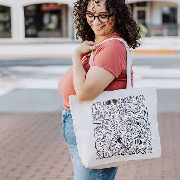 Woman holding What We Carry cotton totebag featuring unique hand illustrated items