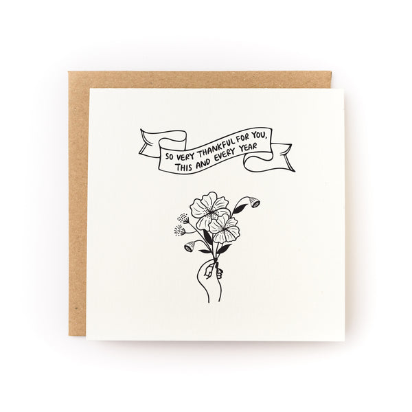 Floral thank you card that has a banner reading "so very thankful for you, this year and every year" with a hand holding a small bouquet of flowers. White card is paired with a kraft envelope.