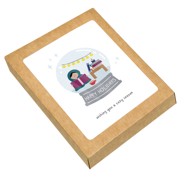 Box set of holiday cards showing a cozy snowglobe scene with a person reading under string lights, a stack of books, and a mug. Ideal for sending warm holiday wishes