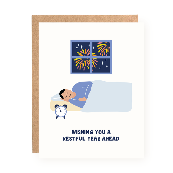 Holiday card showing a man peacefully sleeping in bed as fireworks burst outside the window. Text below reads, 'Wishing you a restful year ahead.' Perfect for sending calm holiday wishes