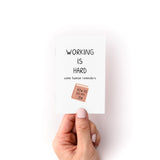 Hand holding the Working is Hard Zine with reminders and a small illustration of a book titled How to Do My Job.