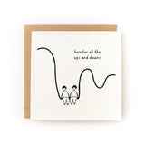 Square white greeting card featuring a minimalist black line drawing of two people holding hands while sitting on a curved line, with the handwritten text "here for all the ups and downs," paired with a brown kraft envelope.