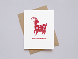 White greeting card with a red goat illustration decorated with floral patterns and the words "Happy Lunar New Year" in red, accompanied by a kraft paper envelope on a light background.