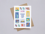 Greeting card designed with colorful illustrated postage stamps featuring New York City landmarks and icons such as the Statue of Liberty, Empire State Building, Brooklyn Bridge, taxi, pizza slice, street food cart, and hot dog, with "Sending Love From NYC" text in the center, set against a white background with a brown kraft envelope underneath.