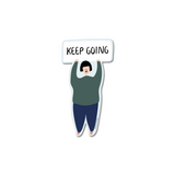 Keep Going Sticker featuring an illustrated figure in a green sweater and blue pants holding up a white rectangular sign with motivational text, designed as a die-cut vinyl sticker with white border for laptops, water bottles, and notebooks