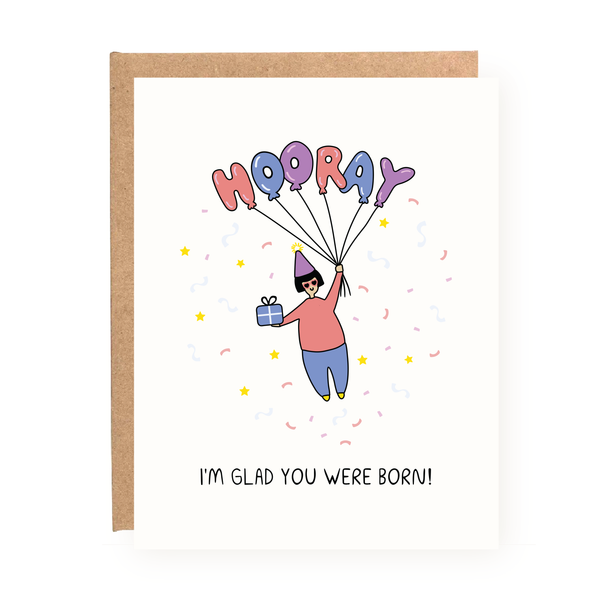 I'm Glad You Were Born Birthday Card with person holding balloons spelling Hooray and holding a gift on white background.