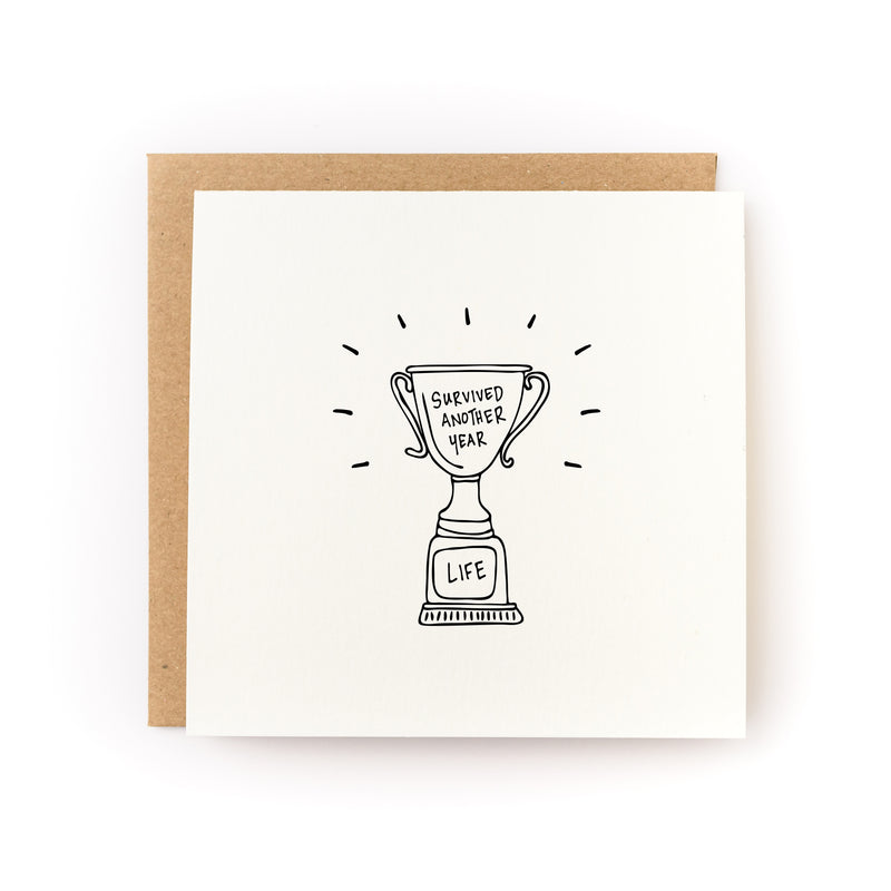Thoughtful sympathy card or encouragement card for a survivor or anyone who is going through a tough time. The card has a white background and black illustration of a trophy that says, Survived Another Year. 