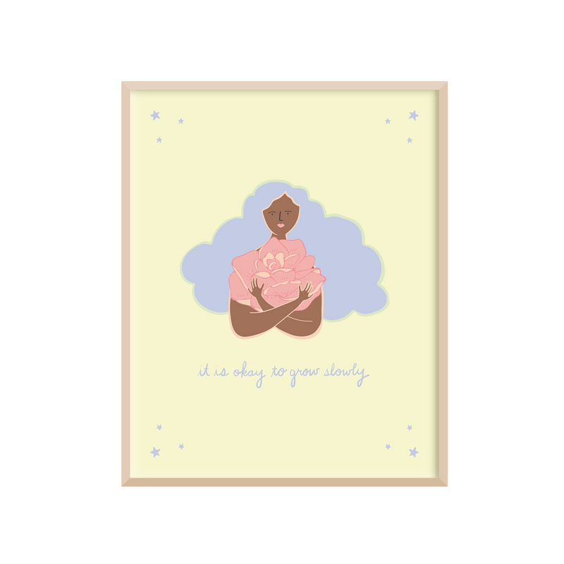 8 x 10 positive affirmations art print with the gentle reminder "It's Okay to Grow Slowly" handwritten underneath hand drawn illustration a woman with curly hair hugging a giant pink rose. The artwork is printed on a light yellow background with blue, pink, and brown illustrations.