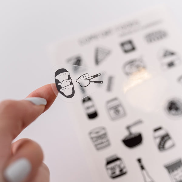 Photo of a hand holding a cute clear sticker.  The sticker has an illustration of  dumplings