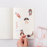 Photo of a hand holding a cute vinyl sticker.  The sticker has an illustration of  a woman relaxing.