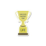 Survived Another Year Trophy Sticker featuring a yellow trophy design with 'SURVIVED ANOTHER YEAR' text on top and 'LIFE' on the base, die-cut with white border, perfect for laptops and water bottles