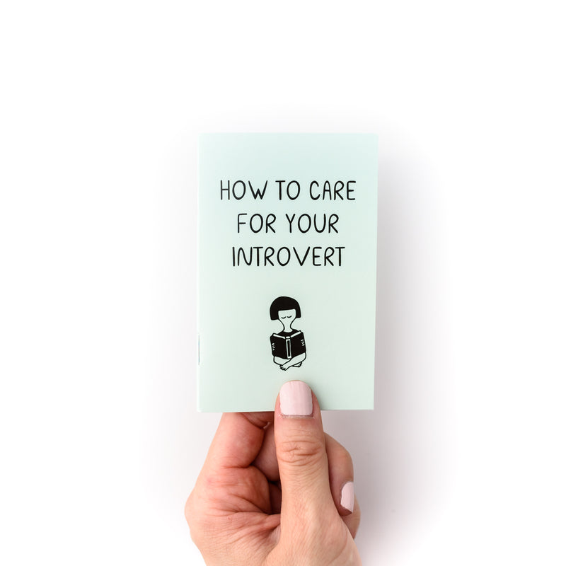 Hand holding small mint green booklet, which is a fun how to guide titled "How to care for your introvert"