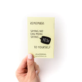 Hand holding a small yellow closed book with the back cover saying "Remember: Saying no can saying yes to yourself"